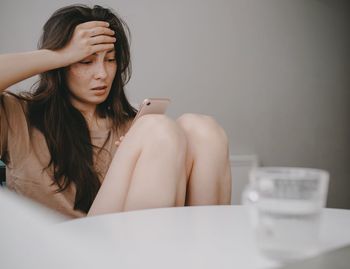 Sad woman with the mobile phone at home in the kitchen by morning