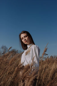 Smiling young woman in white blouse standing in field of dry pampas grass in front of sky