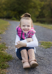 Portrait of cute smiling girl hugging knees while sitting on road