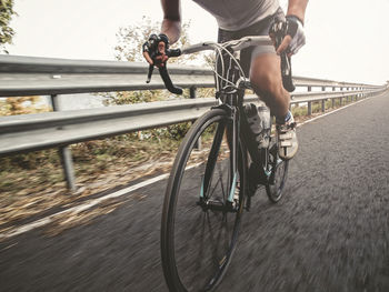 Low section of man riding bicycle on road by railing