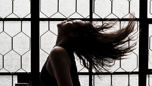 Side view of woman tossing hair by window