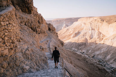 Rear view of man walking on rock in mountains