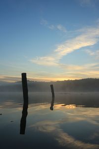 Silhouette wooden posts in lake against sky during sunset