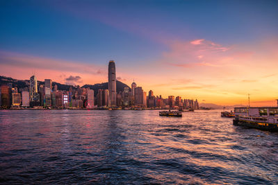 Sea by buildings against sky during sunset