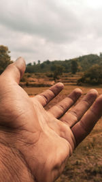Cropped image of man hand against cloudy sky