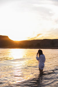 Rear view of woman standing at beach during sunset