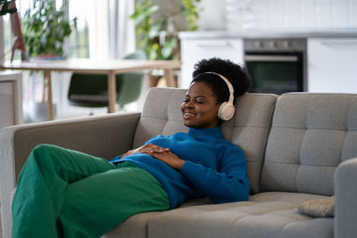 Resting casual african american girl in headphones with slight smile and closed eyes on couch