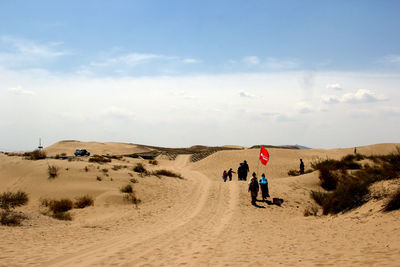 People with flag walking on desert against sky