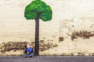 Full length of woman sitting against brick wall