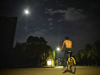 Rear view of man riding bicycle at night