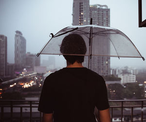 Rear view of man standing against cityscape during rain