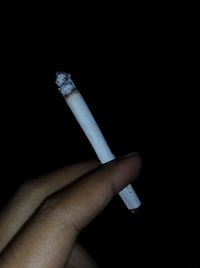 Close-up of hand holding cigarette against black background