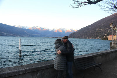Couple kissing while standing by retaining wall against lake