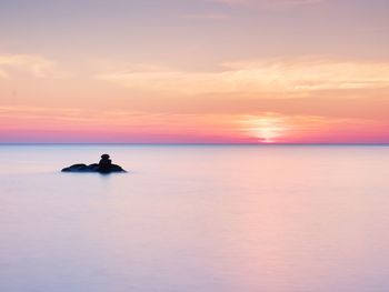 Romantic morning at sea. big boulders sticking out from smooth sea. pink horizon with first sun rays