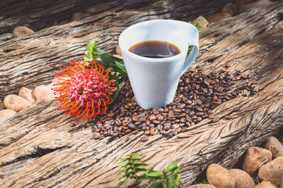 High angle view of coffee cup with flower and roasted beans on wood