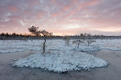 Snow covered landscape against sky during sunset