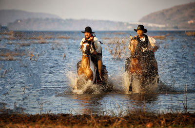 Men wearing costumes riding horses in lake against sky