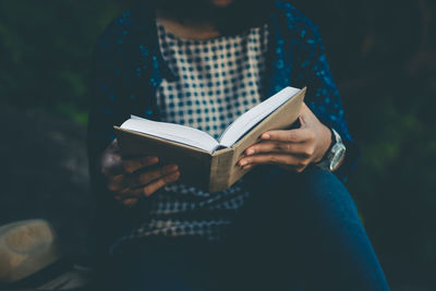 Midsection of woman reading book while sitting outdoors