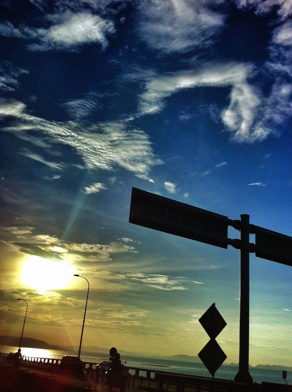 sky, low angle view, silhouette, cloud - sky, sunset, built structure, street light, cloud, cloudy, dusk, outdoors, guidance, nature, no people, sunlight, architecture, beauty in nature, building exterior, blue, dramatic sky