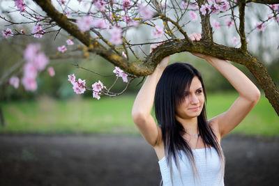 Young woman standing below pink flowers
