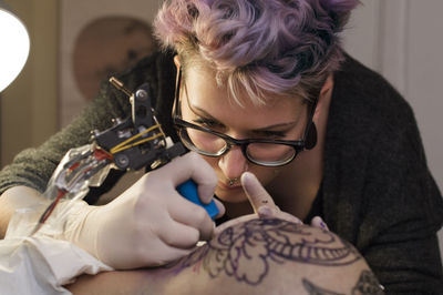 Female tattoo artist tattooing head of client in studio