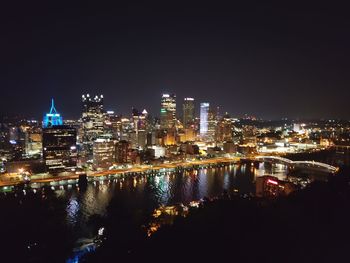 Illuminated buildings by river against clear sky at night