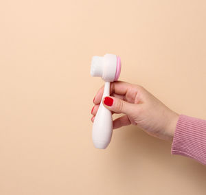 Cropped hand of woman holding bottle against pink background