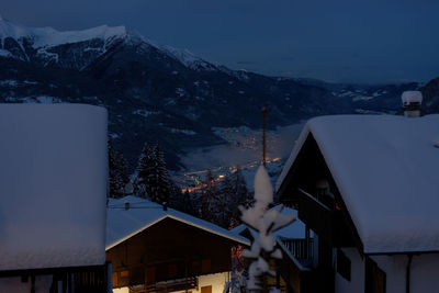 Houses by snowcapped mountains against sky at dusk