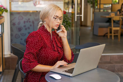 Beautiful woman works on laptop in coffee shop and using mobile phone in a red