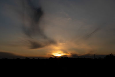 Silhouette trees on field against dramatic sky during sunset