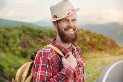 Portrait of a sly cheerful bearded jewish man hitchhiker in a hat and shirt against the backdrop 