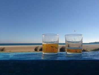 Close-up of glasses on beach against clear blue sky