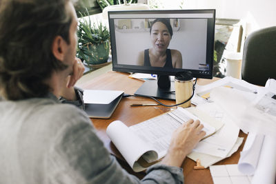 Male architect on video call with female coworker through computer at home office