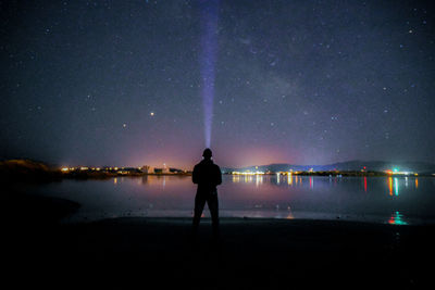 Silhouette man standing by lake against sky at night