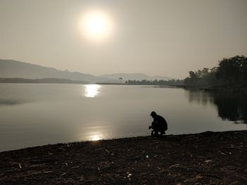 Dog on lake against sky during sunset