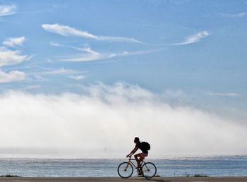 Side view of mature man riding bicycle at beach against sky