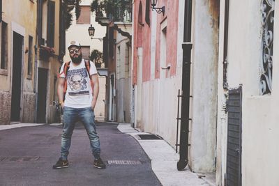 Full length of man in sunglasses standing on road amidst buildings