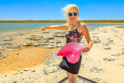 Full length portrait of woman pointing while standing on shore against sky