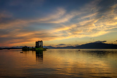 Scenic view of lake by building against sky during sunset