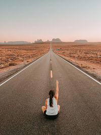 Rear view of woman sitting on road against sky during sunset