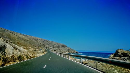 Road by sea against clear blue sky