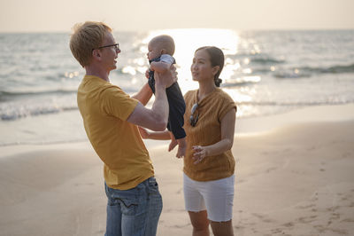 Cheerful family standing on beach with baby against sky