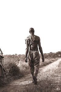 Rear view of man walking on field against clear sky