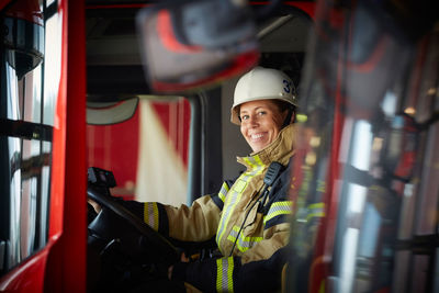 Portrait of smiling female firefighter sitting in fire truck at fire station