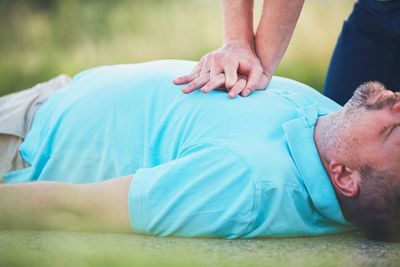 Cropped hands of man resuscitating friend lying on road