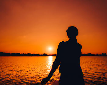 Silhouette man standing by sea against orange sky