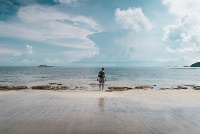 Rear view of man standing on beach against sky