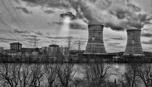 Smoke stacks by river against sky