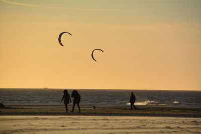 People walking at beach against sky during sunset