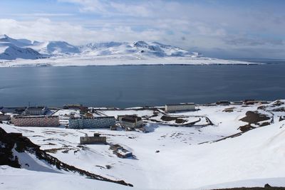 Scenic view of sea by snowcapped mountains against sky